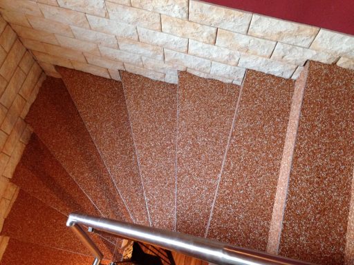 Braune Steinstufen mit Handlauf, die nach unten führen, vor einer wandverkleideten Oberfläche.